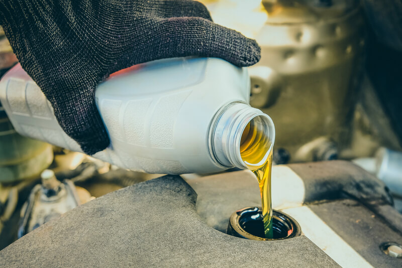 Auto mechanic pouring new engine oil in an engine