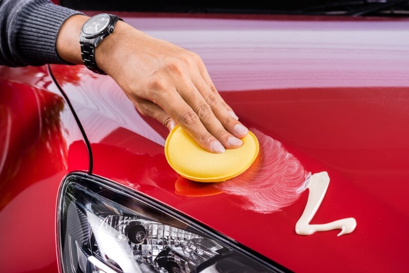 Man applying liquid car wax on a red car