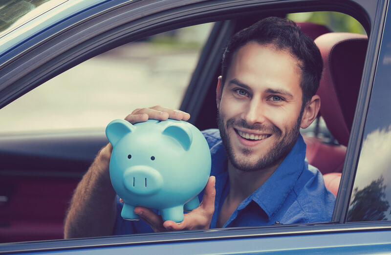 Man sitting in a car holding a blue piggy bank